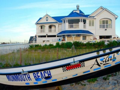 Large beachfront home with dunes with a small sailboat in the forefront .
