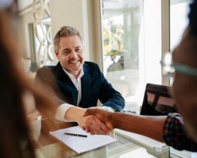 real estate agent behind a desk, shaking the hand of a client