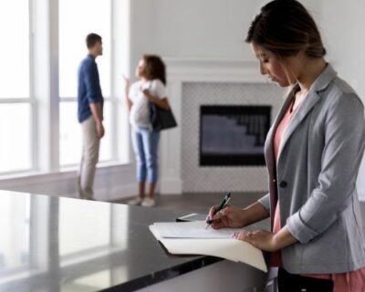 real estate agent writing contract with couple in background 