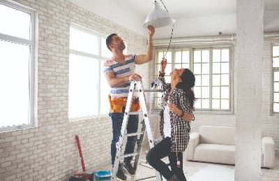 Couple on ladder hanging a ceiling lamp