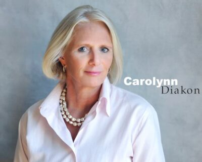 A photo Carolynn Diakon in a collared, white button down shirt and wearing a double strand of pearls.